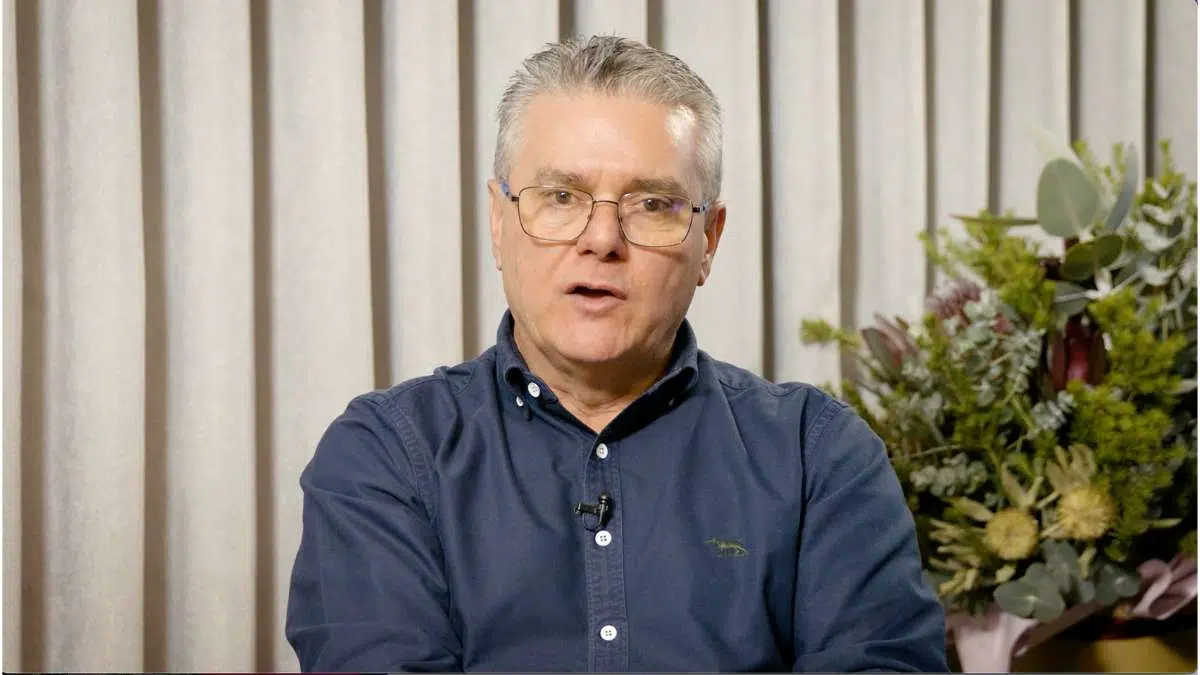 Don't fade into your background Male exec talking to camera. He's wearing a blue shirt to contrast with light coloured walls behind him