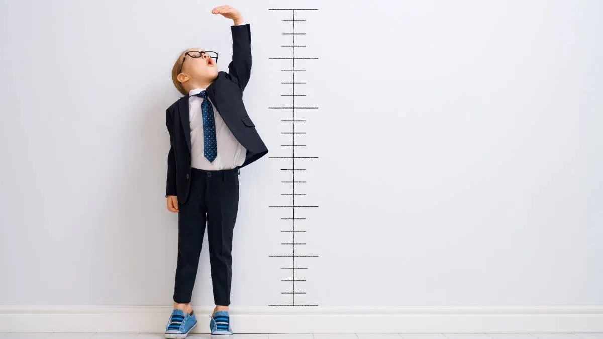 Measuring-success Boy dressed as businessman standing against wall to measure his height success