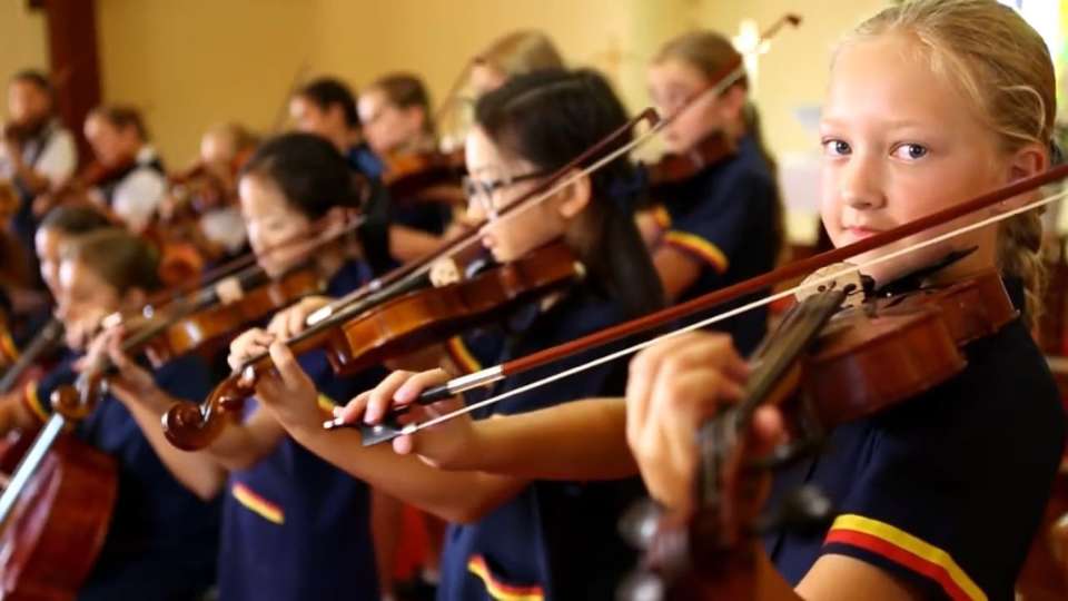 Thumbnail of school students playing instruments, with girl in foreground looking to camera